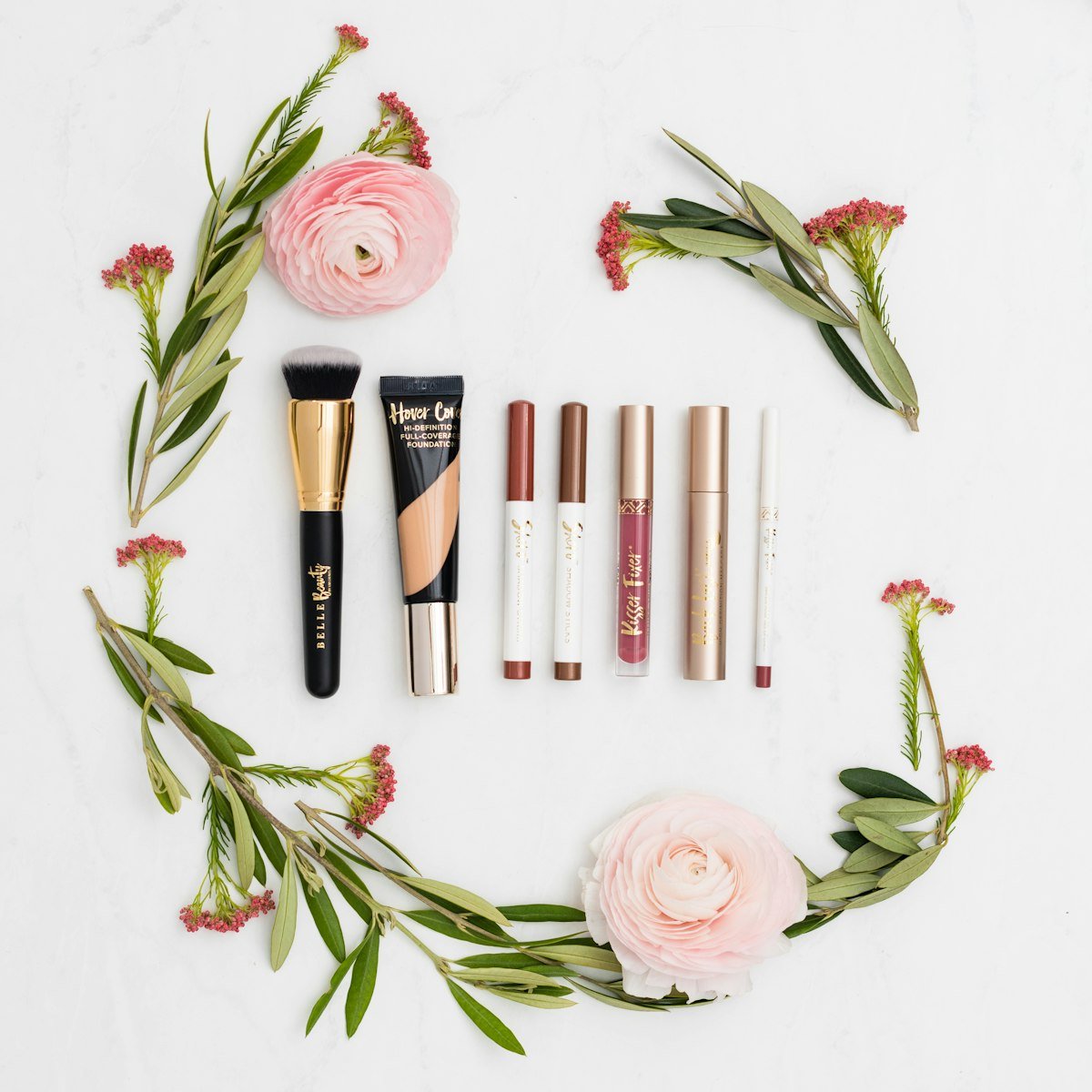 Bridal makeup essentials arranged with blush roses and greenery